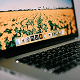 Close-up of a laptop screen showing a yellow flower field wallpaper with application icons