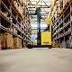 Forklift driving down an aisle in a warehouse between shelves with boxes