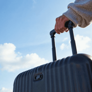 A person holding a suitcase against a background of blue sky with clouds